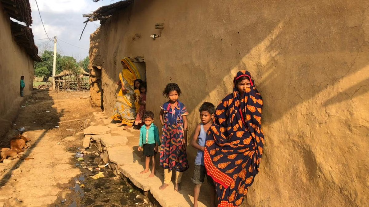 A group of children and a woman outside a mud-walled house in rural India