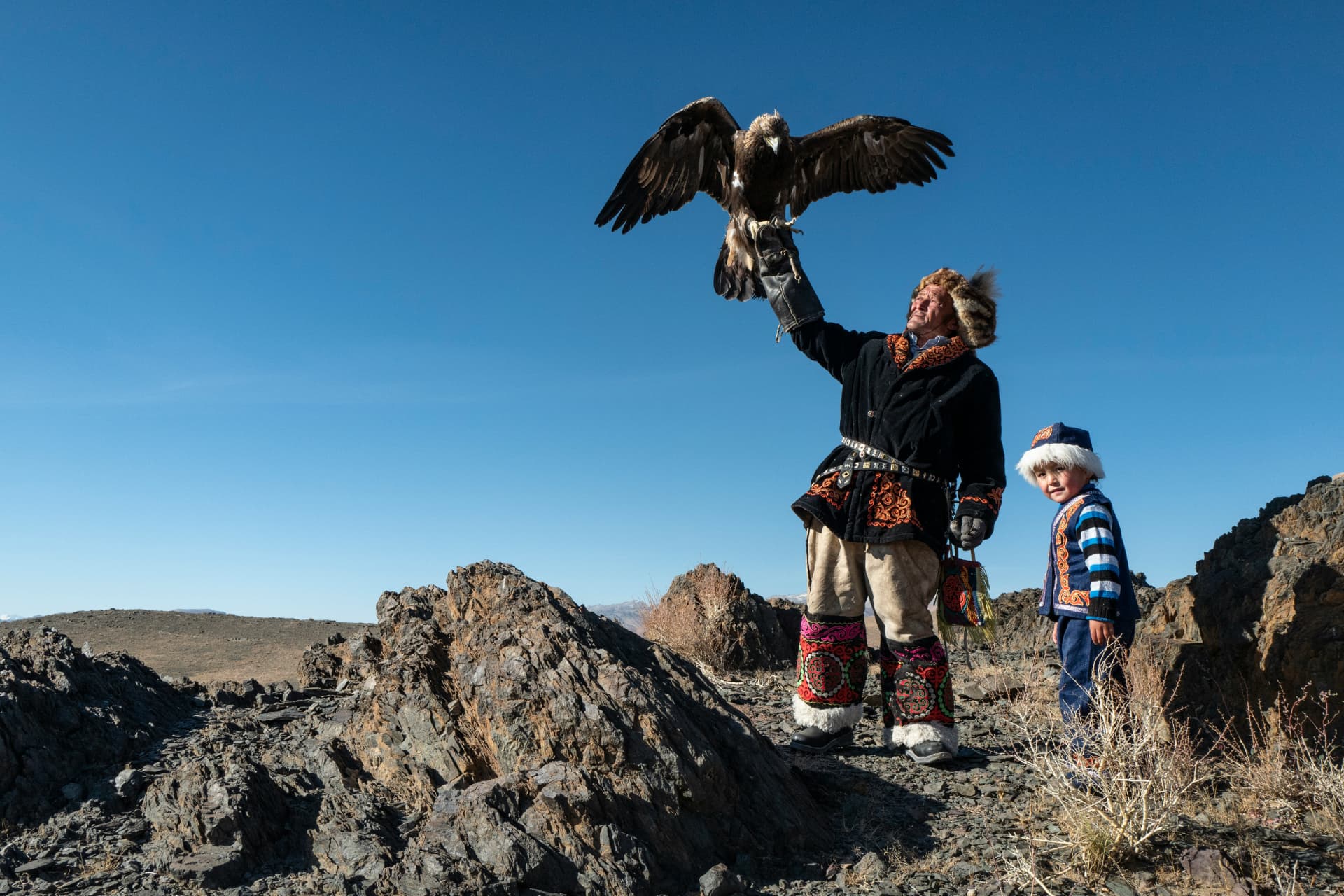 An eagle hunter and a child on a rocky mountain plateau