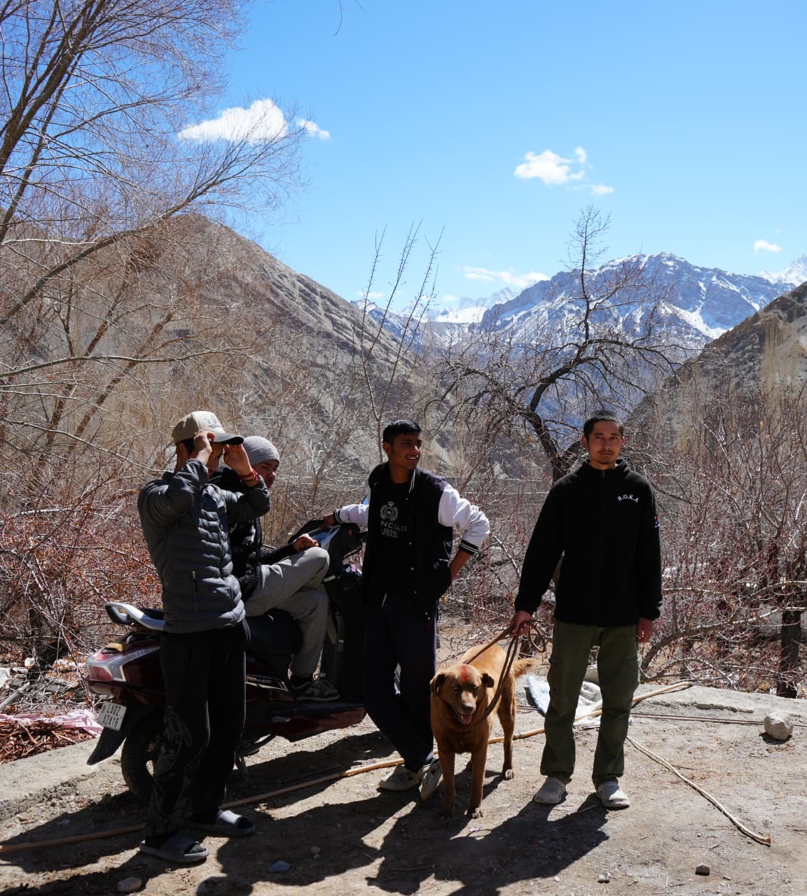 Young men with a dog in a Ladakhi village below snowy peaks